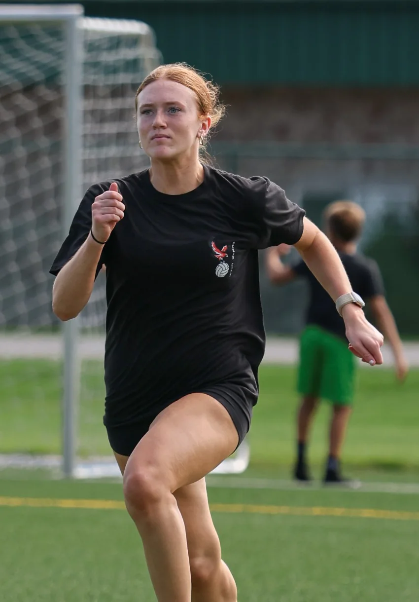 A high-school girl sprinting on a turf soccer field
