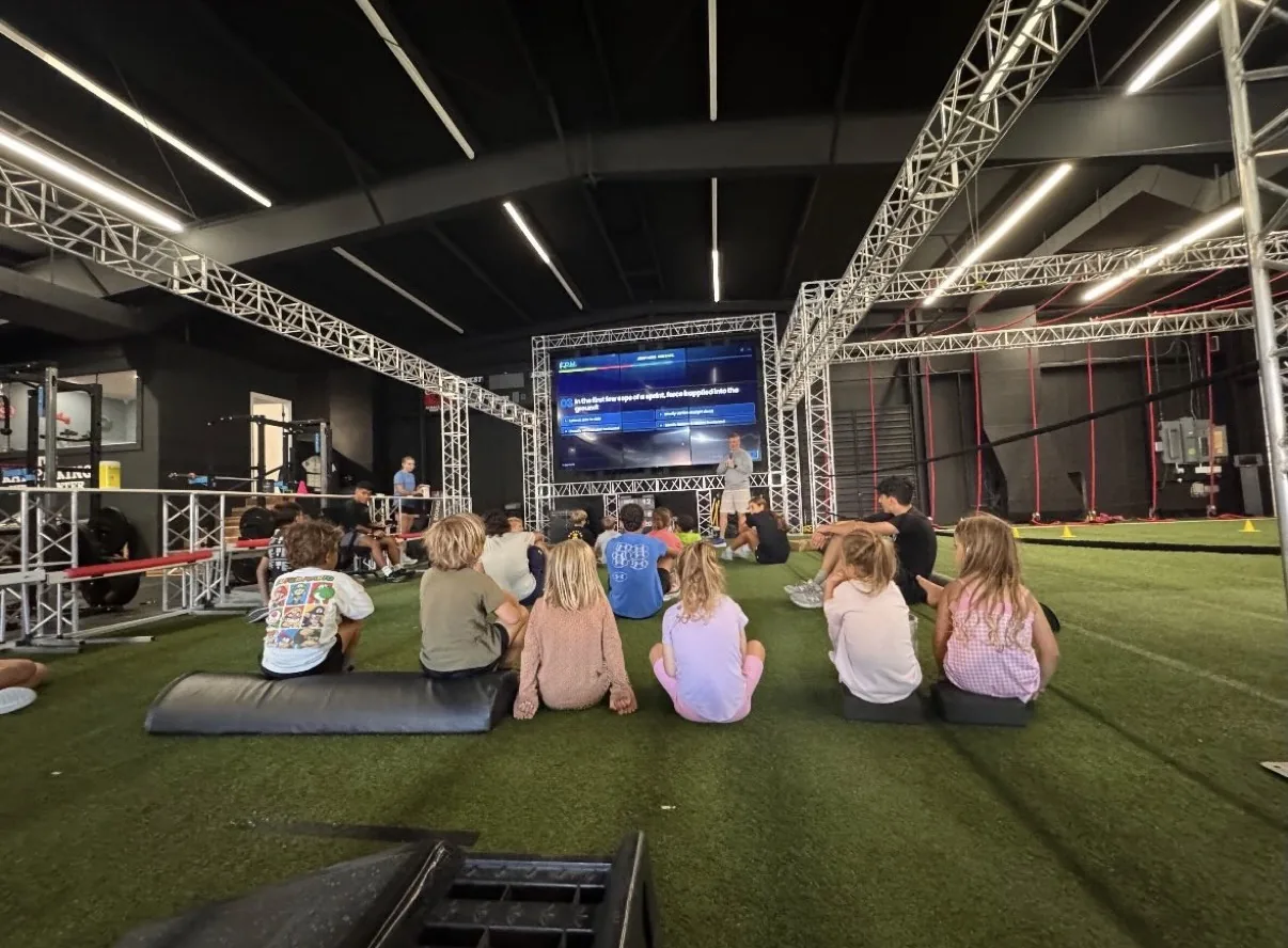 Athletes sitting on the turf at KPM, watching a multiple-choice question on the big screen