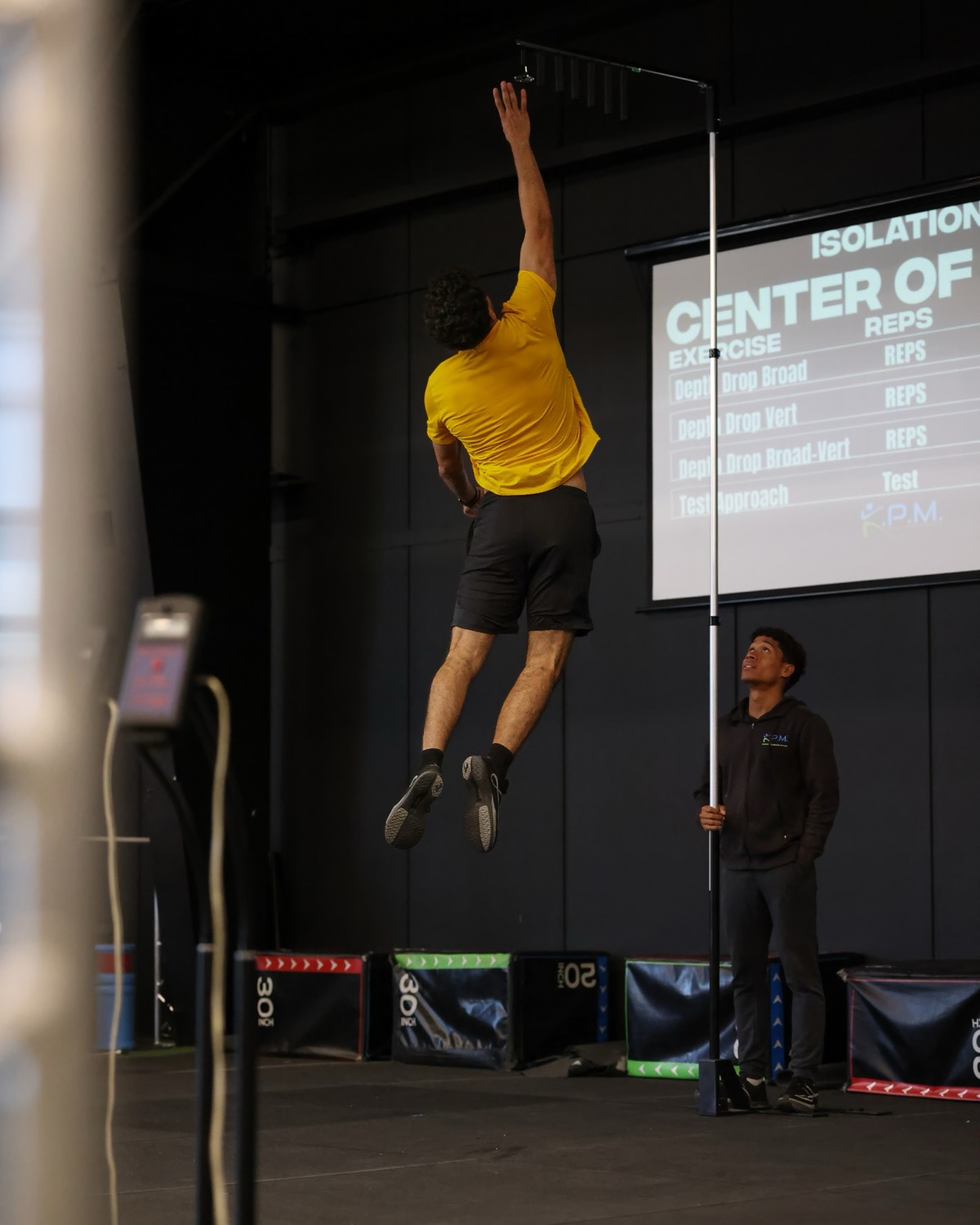 An athlete reaching the top of a vertical jump against the measuring stick